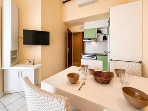 A modern kitchen with a flat-screen TV, a dining table with bowls and glasses, and a wicker chair. - Air-conditioned house near the beach - 6 guests (Saint-Cyprien)