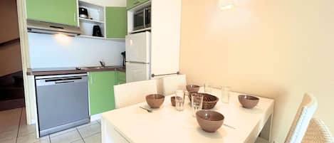 A compact kitchen with a dining area, including a table with bowls and glasses, and a microwave above the counter.