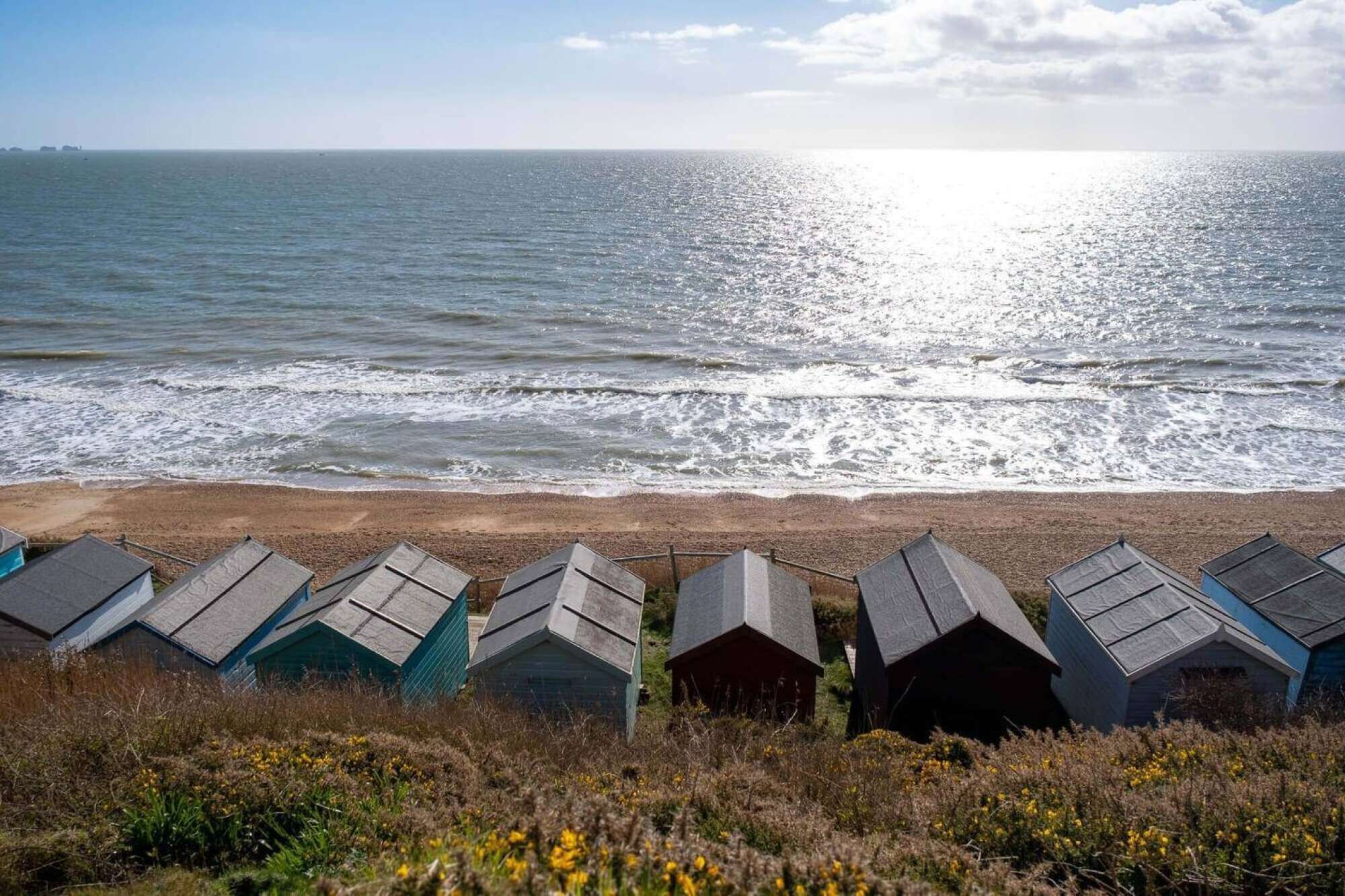 Strandhutten met schuine daken, een zandstrand en de oceaan op de achtergrond.