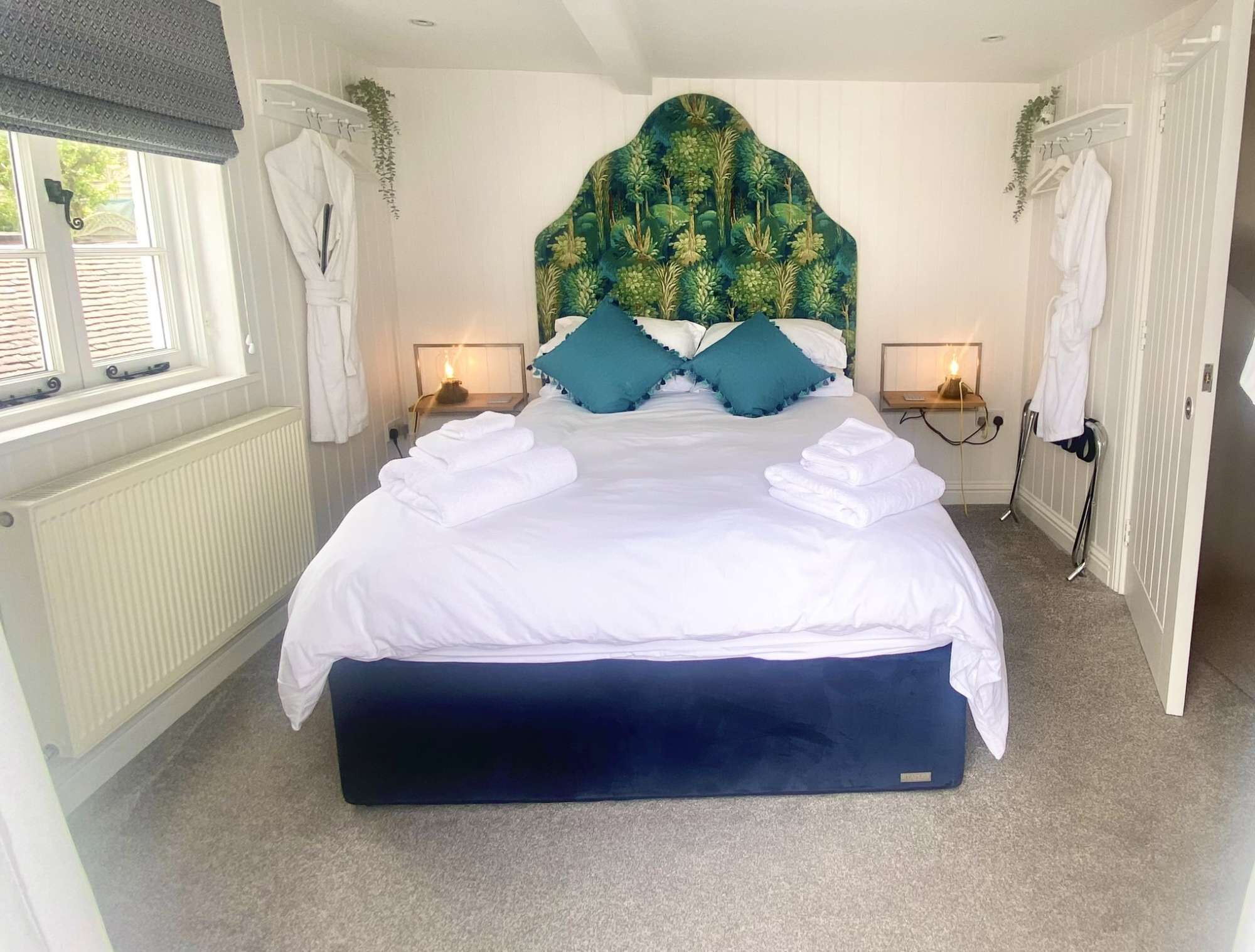 A bedroom with a large bed, two bedside tables with lamps, a radiator, and a window with curtains.