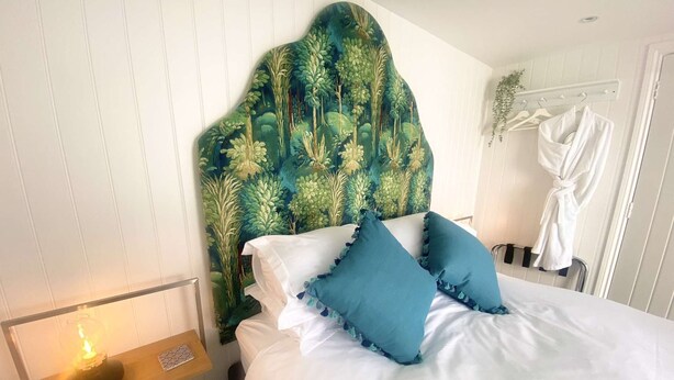 A bedroom with a white bed, teal pillows, and a headboard with a leafy pattern. - Newgate Cottage by NewFo dot Rest (Lymington)