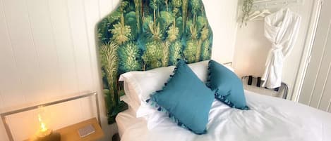 Une chambre avec un lit blanc, des coussins turquoise et une tête de lit ornée d’un motif végétal.