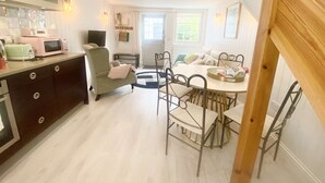 A compact kitchen with modern appliances, a dining area with metal chairs, and a cozy seating area with a chair and a sofa. - Newgate Cottage by NewFo dot Rest (Lymington)