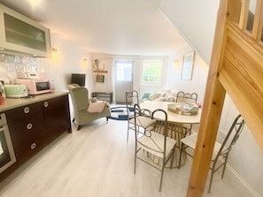 A compact kitchen with modern appliances, a dining area with metal chairs, and a cozy seating area with a chair and a sofa. - Newgate Cottage by NewFo dot Rest (Lymington)