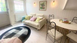 A living room with a white sofa, a round dining table, and a black and white rug. - Newgate Cottage by NewFo dot Rest (Lymington)