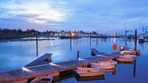 A marina with boats docked at wooden piers, calm water, and a cityscape in the background. - Newgate Cottage by NewFo dot Rest (Lymington)