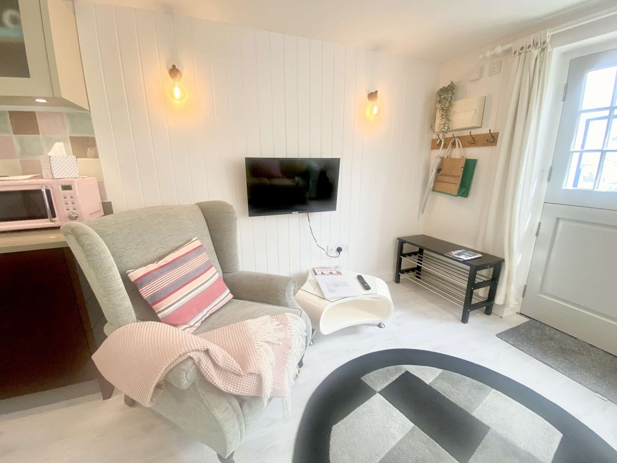 A living room with a sofa, a flat-screen TV mounted on the wall, a small side table, and a window with curtains.