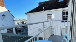 A balcony with a white railing, a small table, and a view of a marina with boats. - Newgate Cottage by NewFo dot Rest (Lymington)
