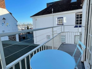 A balcony with a white railing, a small table, and a view of a marina with boats. - Newgate Cottage by NewFo dot Rest (Lymington)