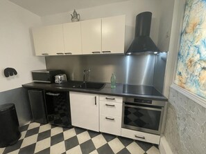 A compact kitchen with white cabinets, a black countertop, a stainless steel range hood, a toaster, and a sink. - Gîte in Touraine, pets welcome - 4 guests (Rochecorbon)
