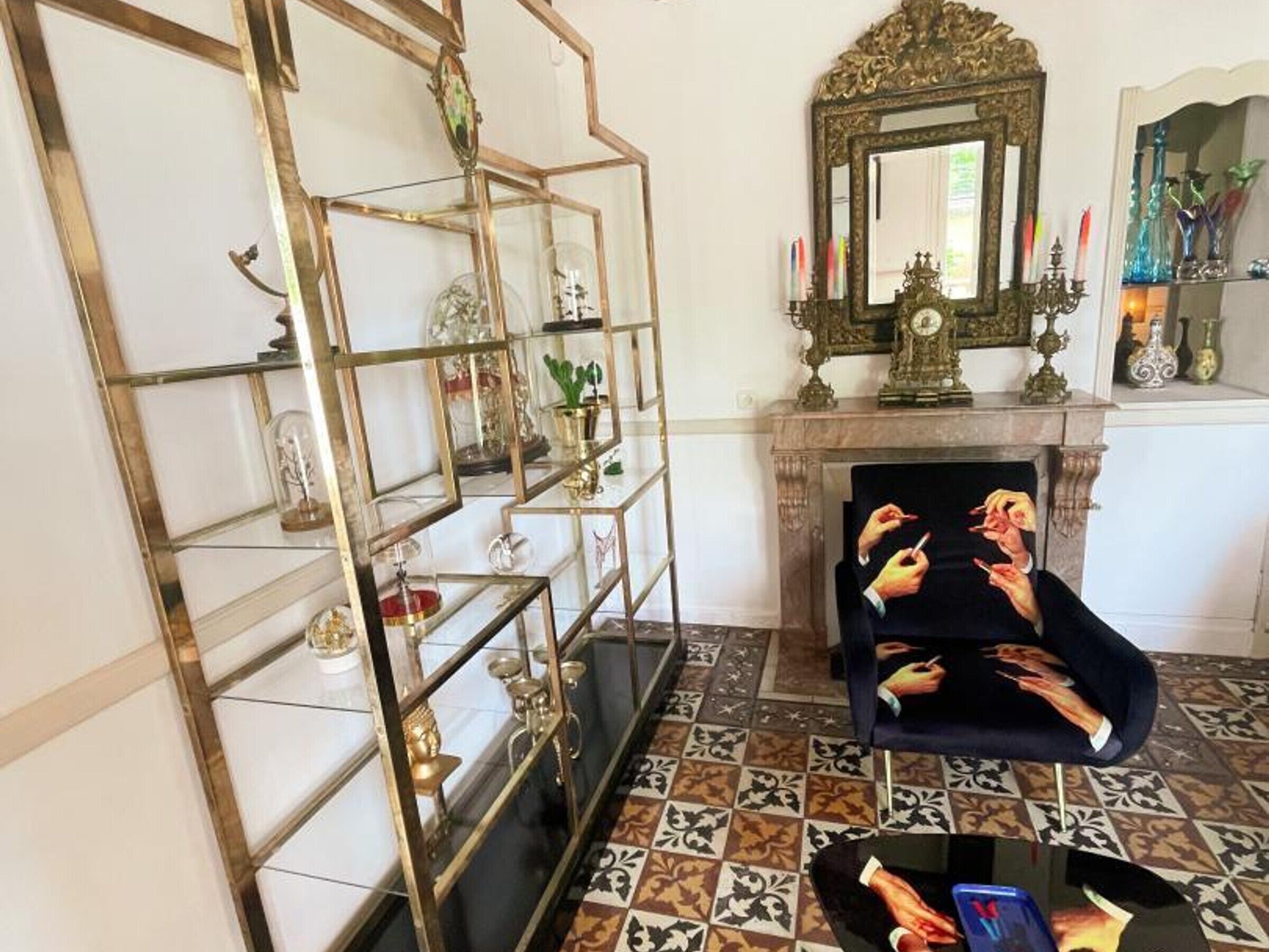 Ein Zimmer mit einem gemusterten Boden, einem Zier-Spiegel, einem Kamin und einem Sessel mit glänzender Oberfläche.
