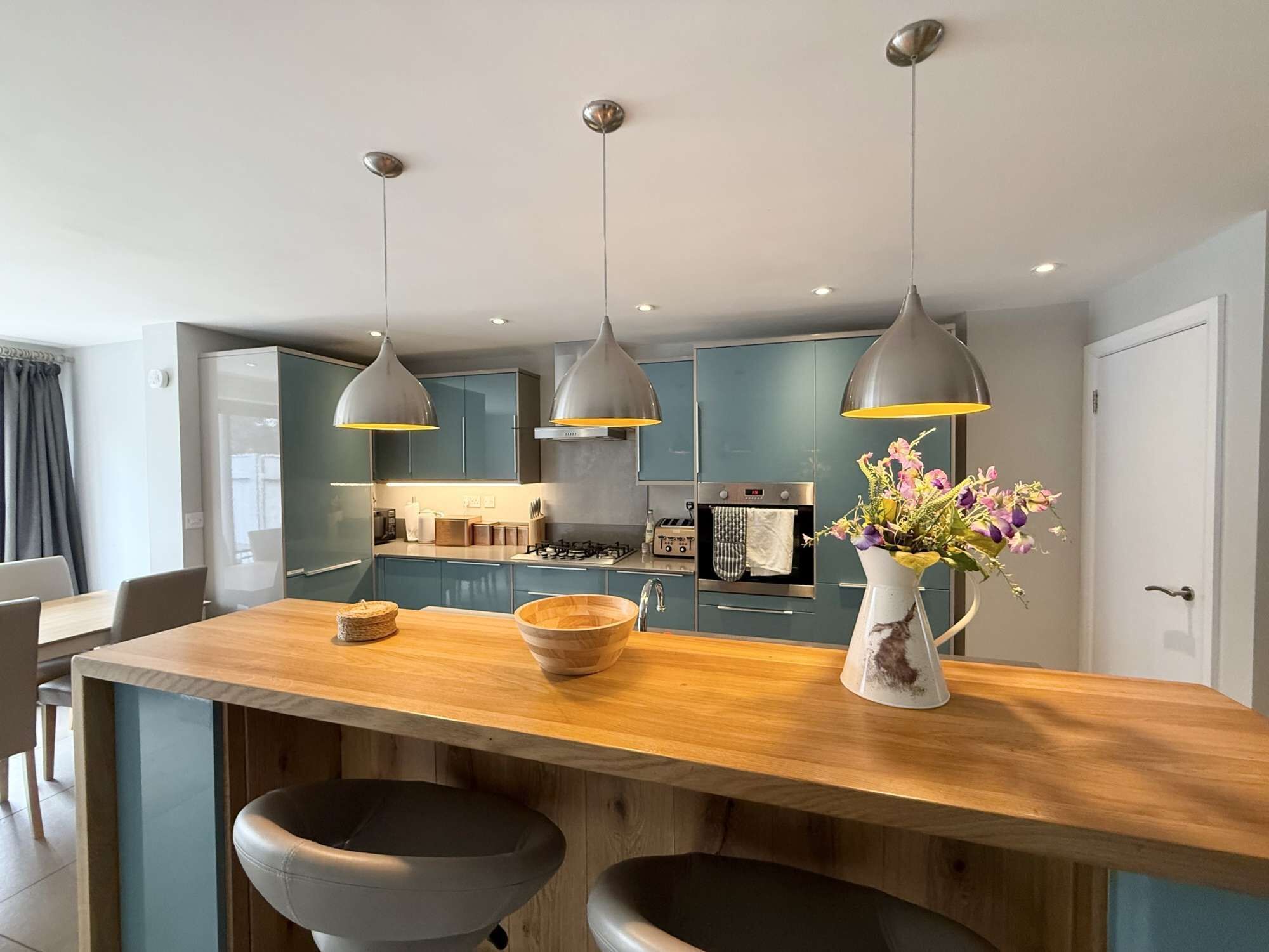 A modern kitchen with a central island, pendant lighting, and a vase of flowers.