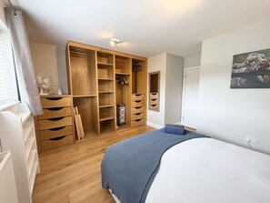 Quarto com uma cama, guarda-roupa de madeira, escrivaninha e janela com cortinas.