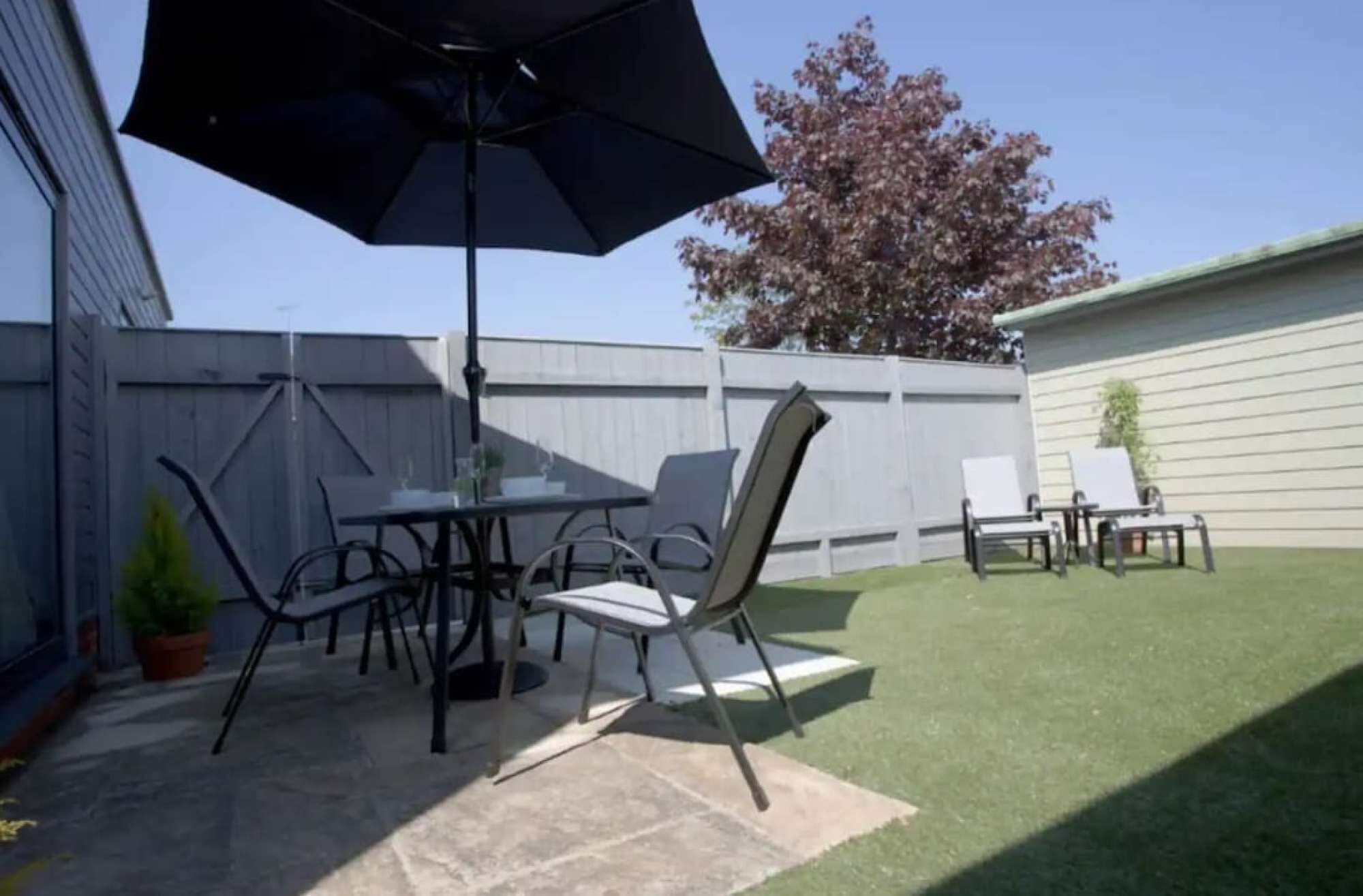 An outdoor patio with a table and chairs, a large umbrella, and a well-maintained lawn.
