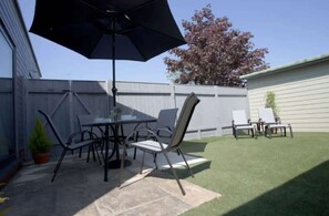An outdoor patio with a table and chairs, a large umbrella, and a well-maintained lawn. - Marigold Cottage by NewFo dot Rest (Brockenhurst)