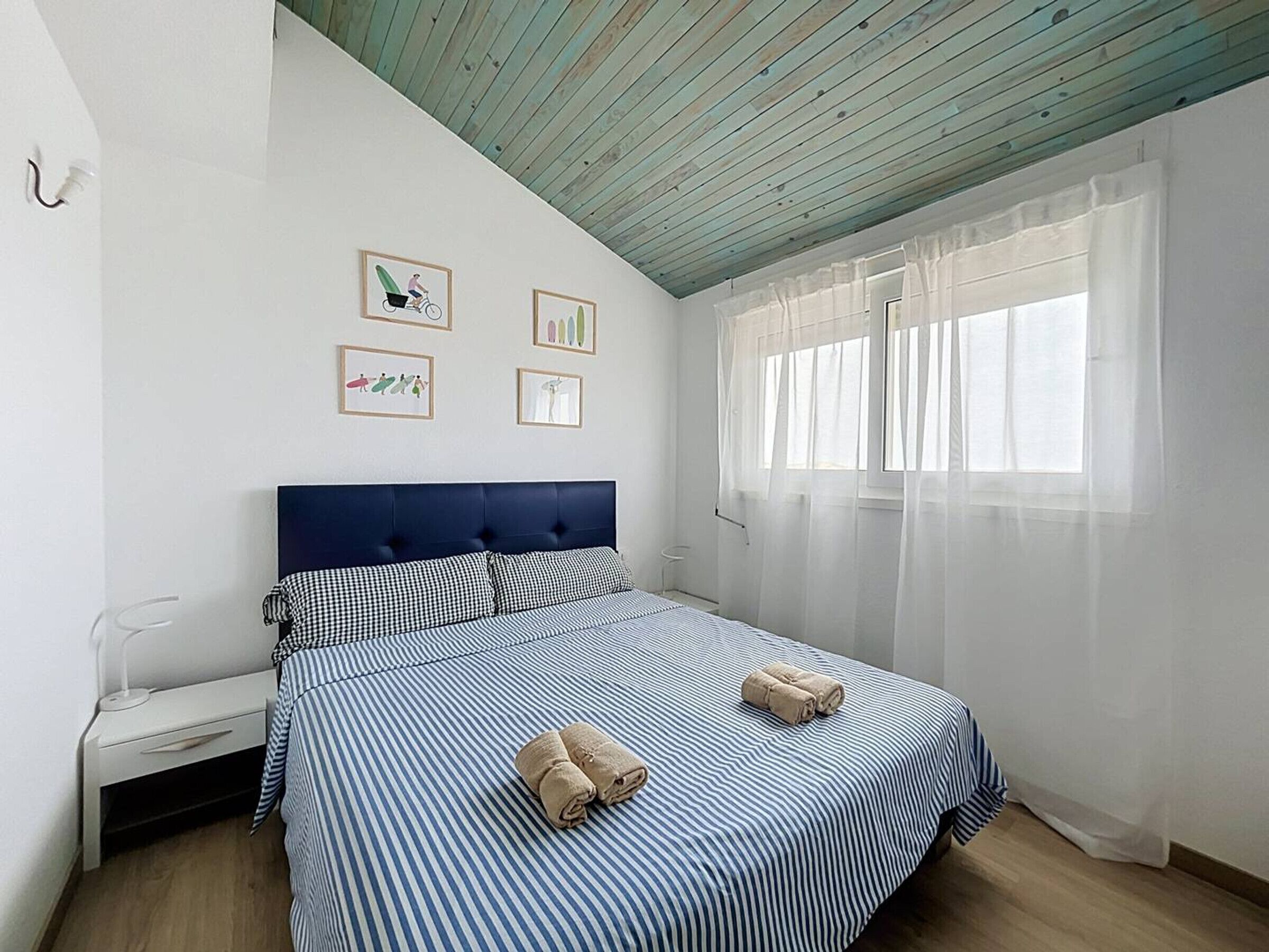 Ein Schlafzimmer mit Bett, Nachttisch, einem Fenster mit Vorhängen und Wandbildern.