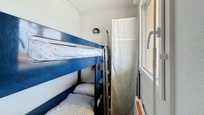 Una habitación pequeña con literas, una ventana con cortina y una puerta con manija.