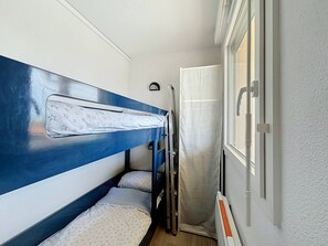 Ein kleines Zimmer mit Etagenbetten, einem Fenster mit Vorhang und einer Tür mit Griff.
