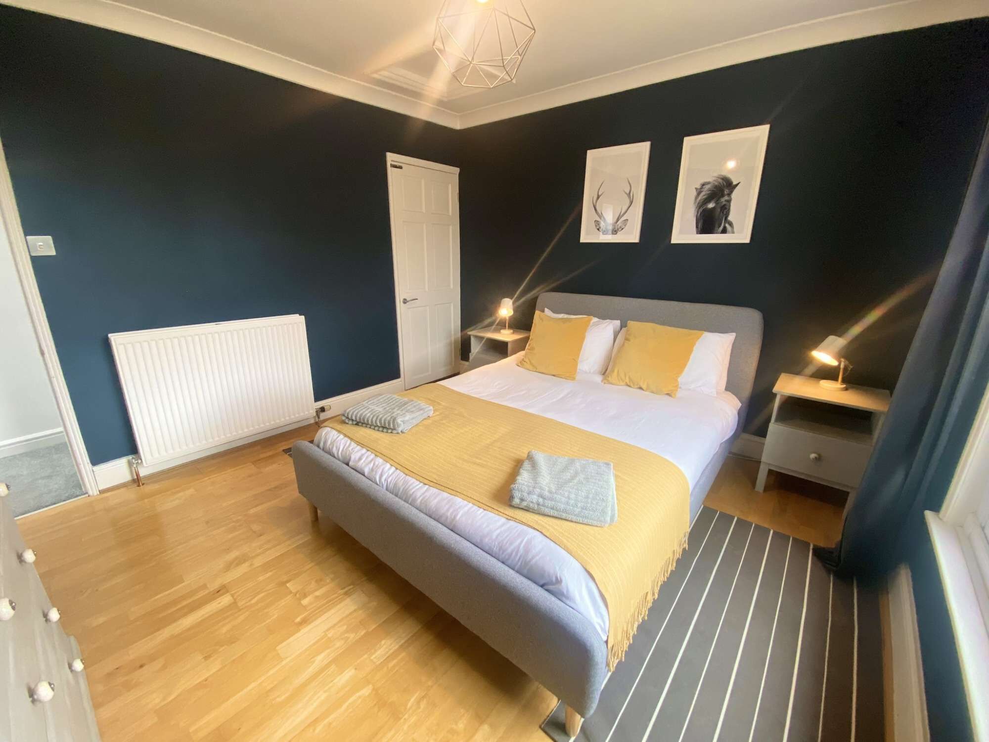 A bedroom with a bed, bedside tables, a radiator, and artwork on the wall.