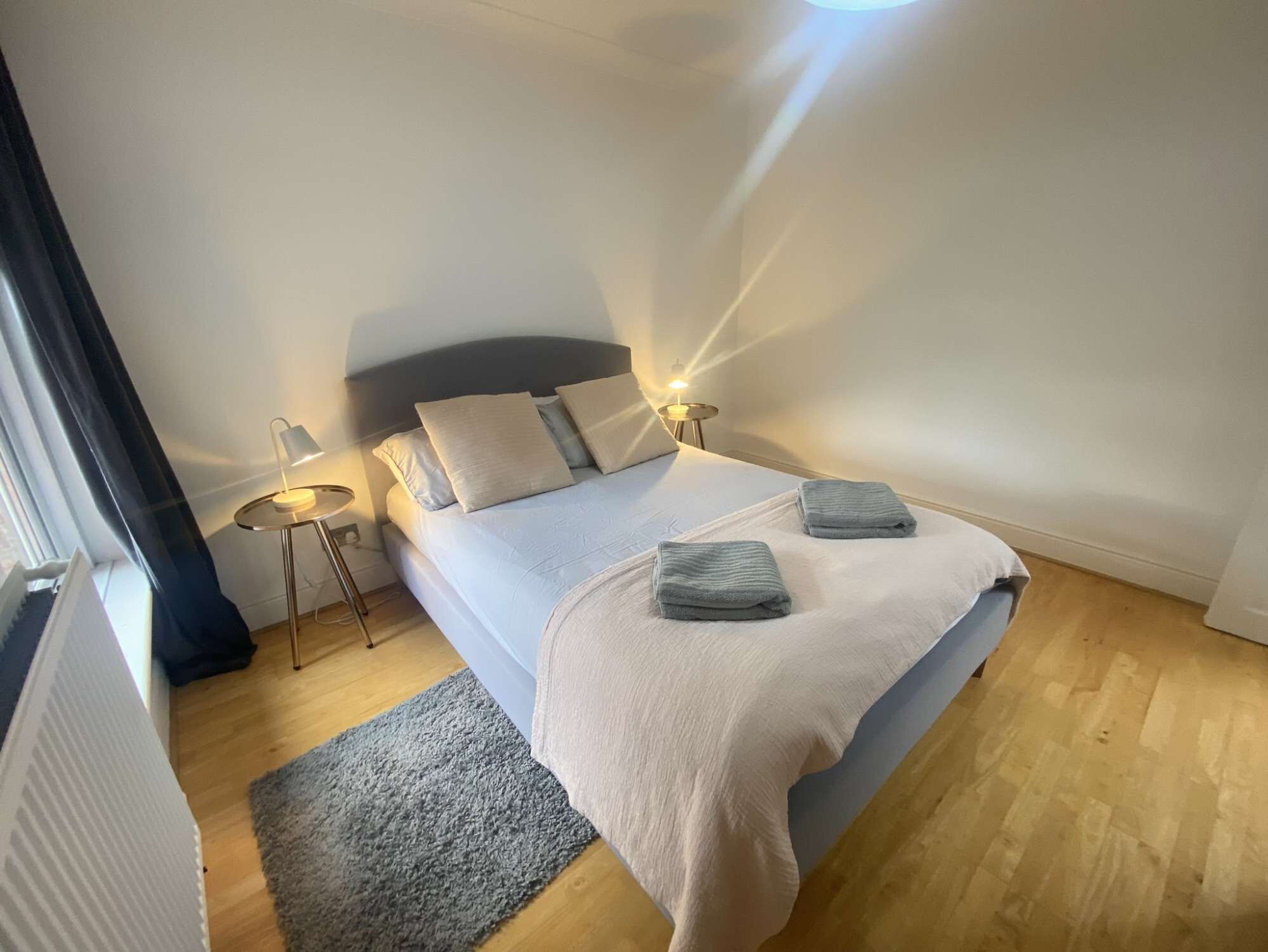 A bedroom with a bed, bedside lamps, a rug, and a radiator.