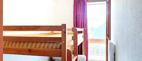 Una cama litera con estructura de madera y una ventana con cortinas.