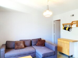 Ein modernes Wohnzimmer mit einem grauen Sofa, einem Holzschrank und einer Pendelleuchte.
