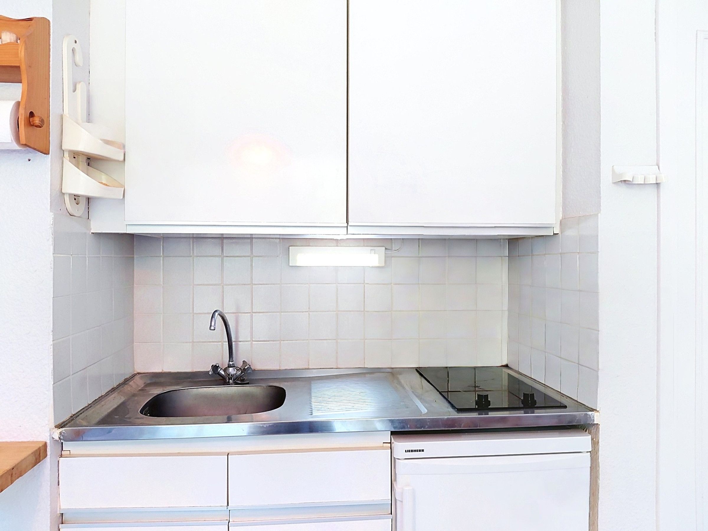 Una cocina con armarios blancos, un lavamanos de acero inoxidable y un lavavajillas.