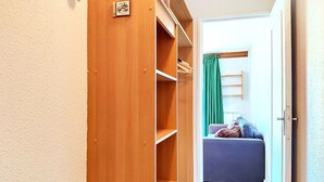 Ein Holzschrank mit Regalen und Kleiderstange, der zu einem Raum mit einer Couch und einem grünen Vorhang führt.