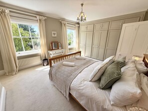Ein Schlafzimmer mit einem großen Bett, einer Kommode, einem Heizkörper und einem Fenster mit Vorhängen.
