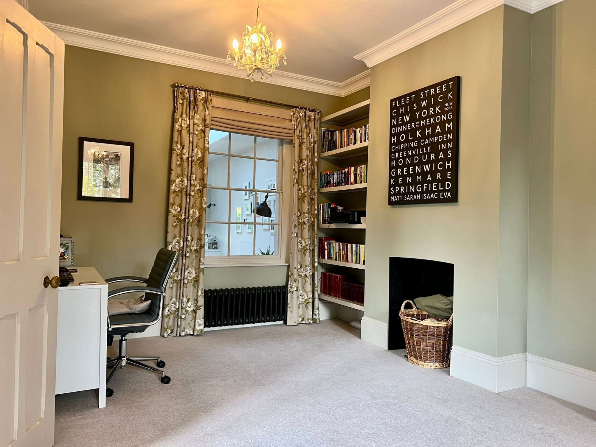 A room with a radiator, a bookshelf, a desk with a chair, a window with curtains, and a chandelier.