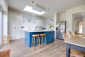 A modern kitchen with a blue island, wooden stools, white cabinets, and a refrigerator with magnets. - Springfield by NewFo dot  rest (Milford on Sea)