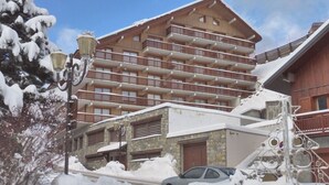 Ein mehrstöckiges Holzgebäude mit Balkonen und einer Steinaußenwand, wobei ein Auto zum Teil im Schnee versunken ist.