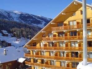 A multi-story wooden building with balconies, surrounded by snow-covered mountains. - Apartment mountain view in center - 6 guests (Méribel)