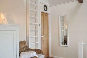 Ein Zimmer mit einem Korbstuhl, einem weißen Schrank, einer Holztür und einem Spiegel an der Wand.