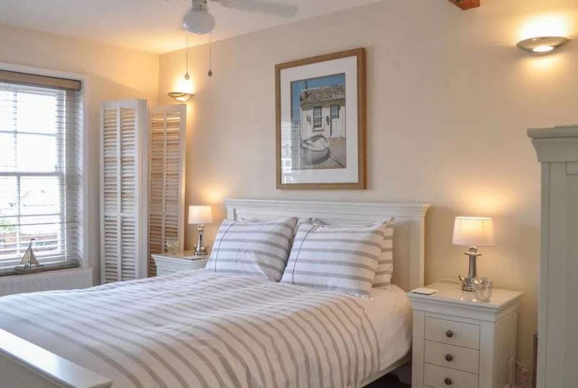 A bedroom with a bed, bedside tables, a framed picture, and a window with shutters.
