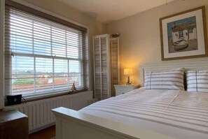 A bedroom with a bed, a nightstand, a lamp, a radiator, and a window with blinds. - Starboard Light by NewFo dot Rest (Lymington)