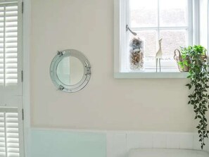 A room with a round mirror on the wall, a window with a view of the outside, and a plant on the windowsill. - Starboard Light by NewFo dot Rest (Lymington)