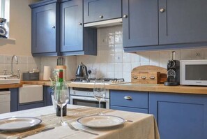 A kitchen with blue cabinets, a wooden countertop, a stove, a microwave, and a dining table set with plates and a wine glass. - Starboard Light by NewFo dot Rest (Lymington)