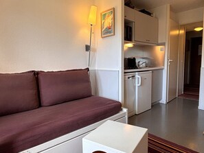 Une pièce compacte comprenant un canapé, une petite table, une kitchenette équipée d’un four à micro-ondes et d’un réfrigérateur.