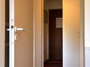 Un couloir avec une porte en bois au fond, un mur blanc et une poignée de porte.