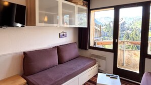 A room with a sofa, a television, a cabinet, and a window with a view of mountains. - Studio cabin, mountain view - 4 guests (Avoriaz)