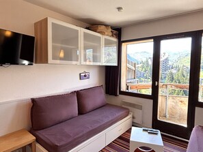 A room with a sofa, a television, a cabinet, and a window with a view of mountains. - Studio cabin, mountain view - 4 guests (Avoriaz)
