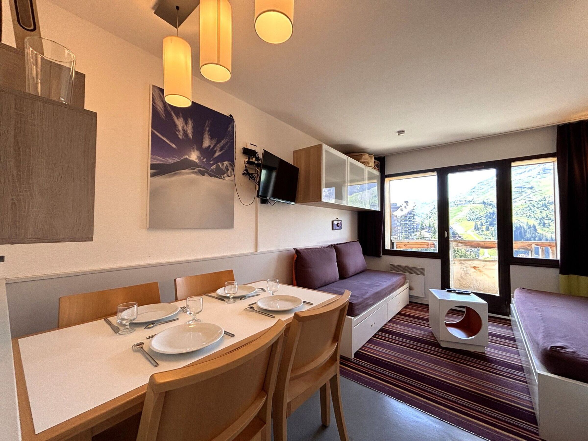 A dining area with a table set for four, a sofa, and a television mounted on the wall.
