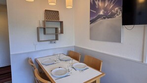 A dining area with a table set for four, wooden chairs, pendant lights, a wall-mounted shelf with glasses, and a framed picture of a mountain landscape. - Studio cabin, mountain view - 4 guests (Avoriaz)