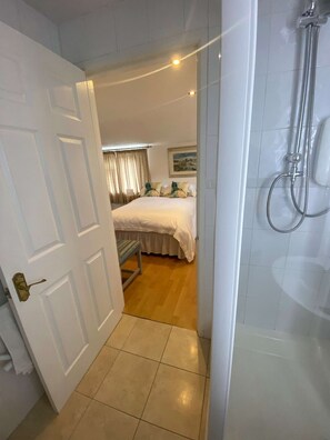 Une chambre d’hôtel avec une douche, un lit avec une literie à motifs floraux et une vue sur le paysage urbain par la fenêtre.