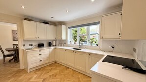 Una cocina moderna con armarios blancos, piso de madera en patrón de espiga y una ventana con plantas.