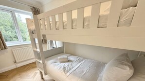 Una cama litera con ropa de cama blanca y un suelo con estampado de espiga.
