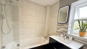 Un baño moderno con ducha envuelta en vidrio, una bañera independiente y un tocador con espejo.