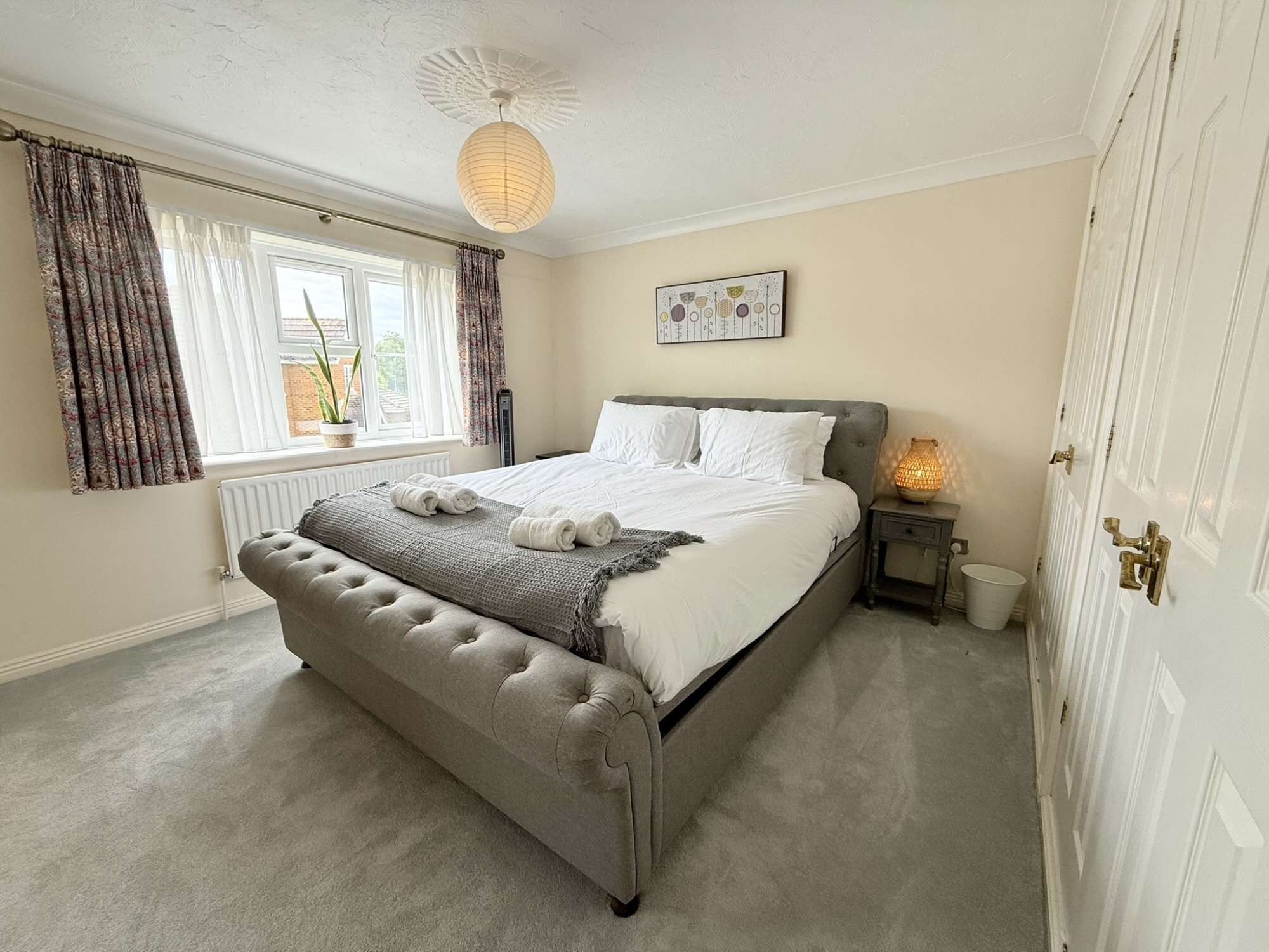 A bedroom with a large bed, a bedside table with a lamp, a radiator, and a window with curtains.