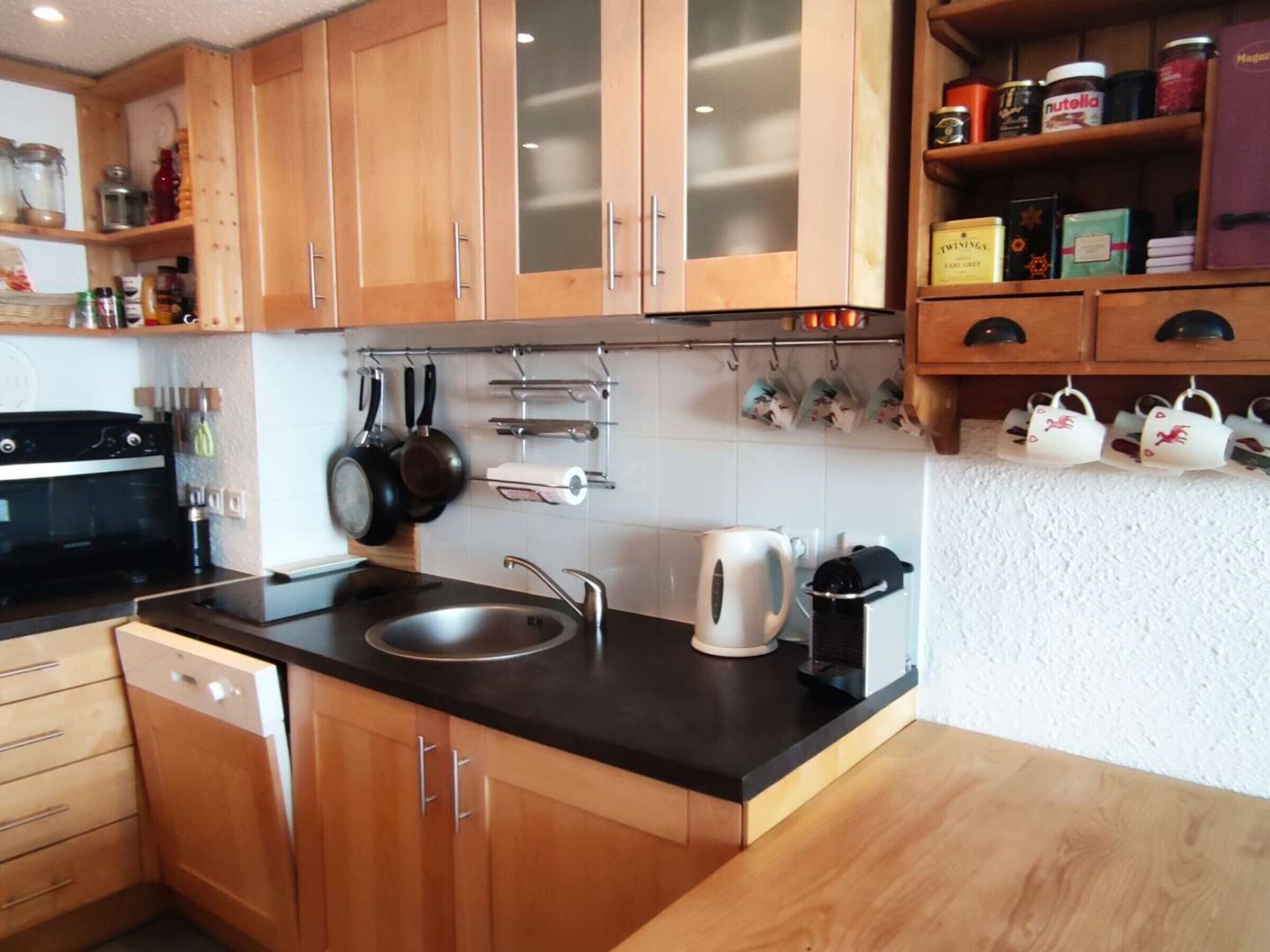A kitchen with wooden cabinets, a black countertop, a kettle, and a coffee machine.